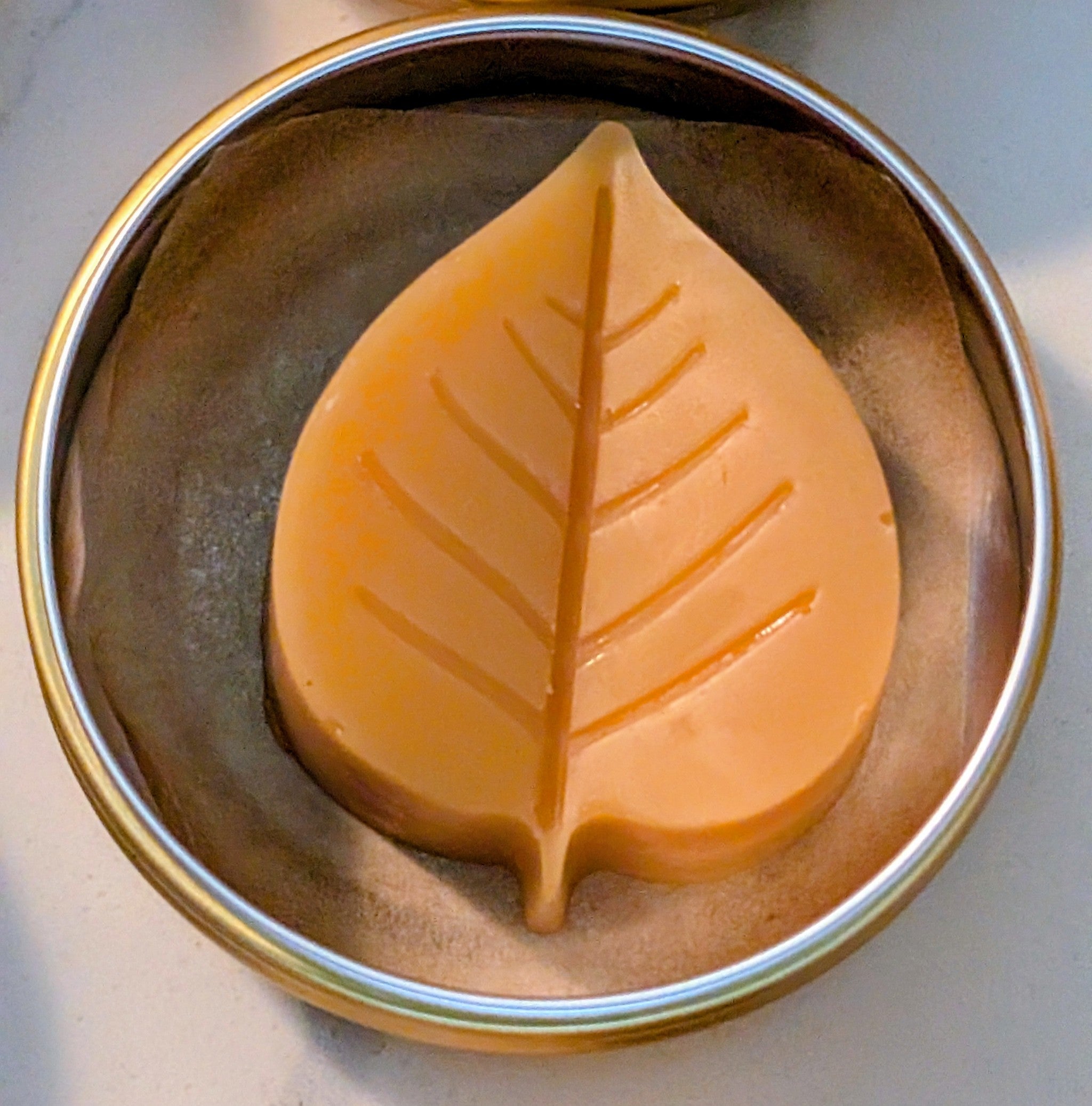 Tin jar of 1 ounce Prakriti Sattva Paduka Lotion bar balm for cracked heels and dry hands in a leaf shape.