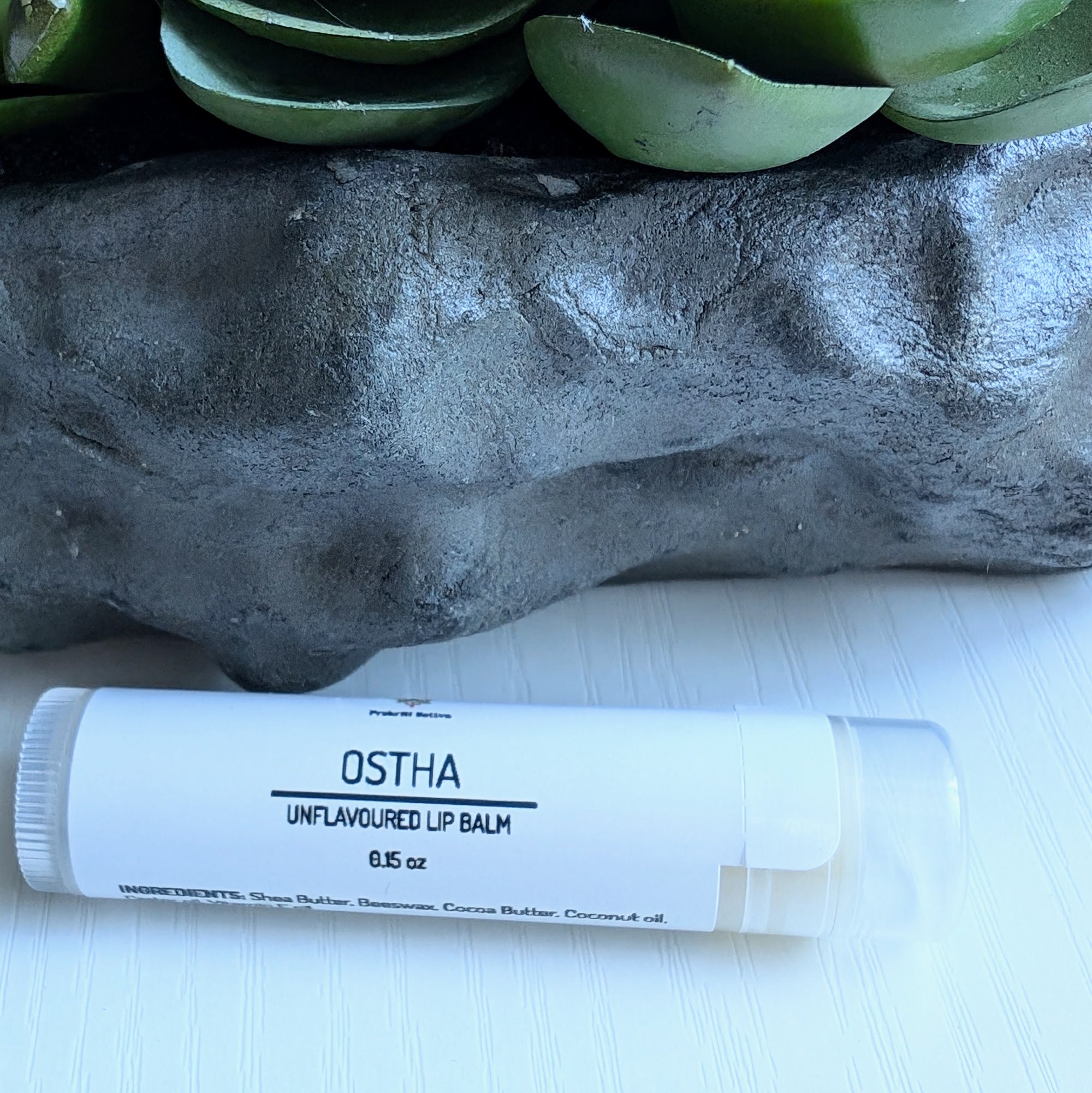 Unflavored natural lip balm with nourishing butters, oils, and beeswax. It is a tube of lip balm with a clear color. The label features Ayurvedic symbols and herbs, indicating the natural ingredients used.