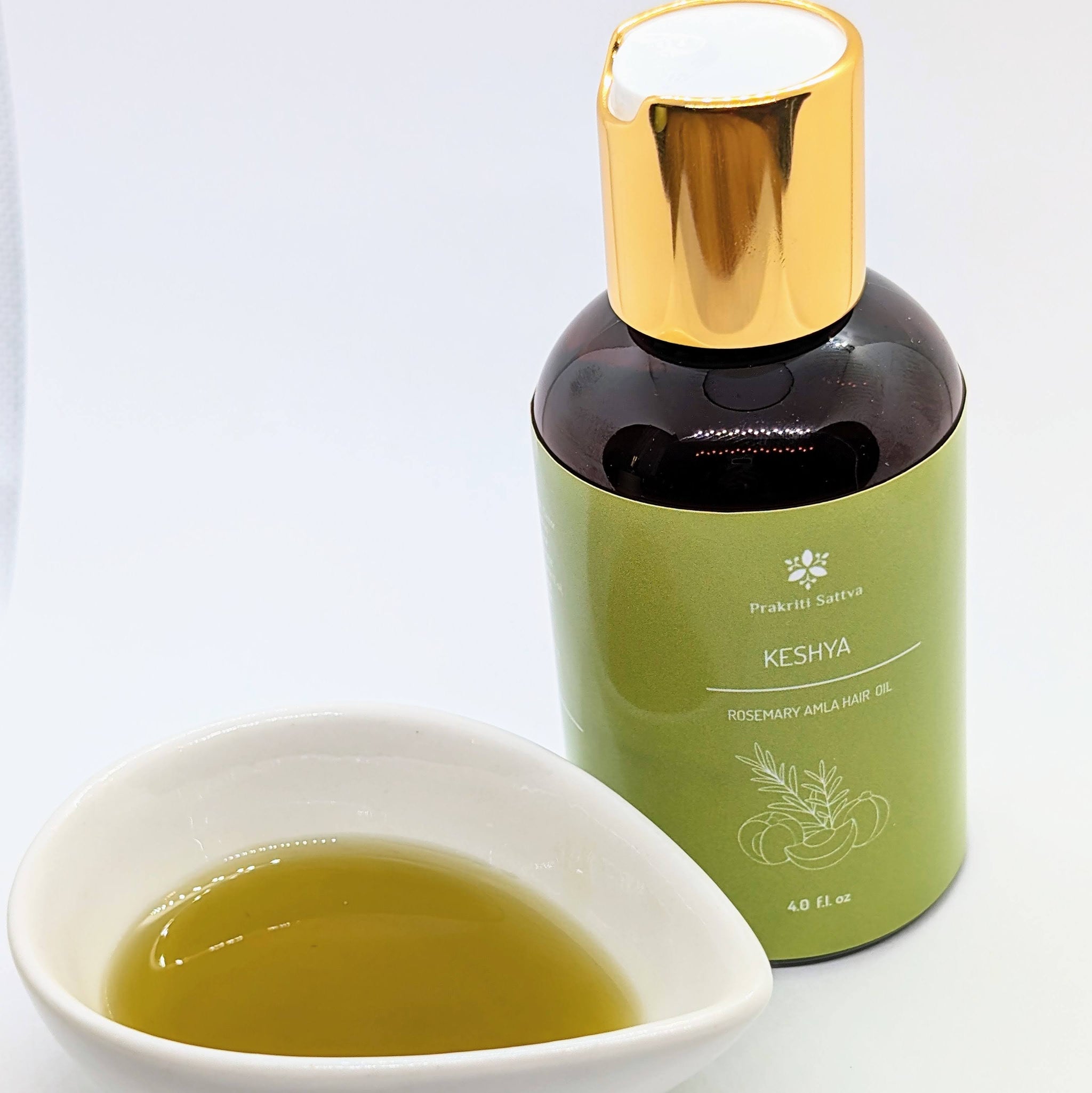 A dark amber bottle filled with Prakriti Sattva Rosemary Amla Hair Oil. A small bowl of the hair oil is next to the 4-ounce keshya rosemary amla hair oil. The label features Ayurvedic symbols and herbs, including rosemary, amla, bhringaraj, and licorice, indicating the natural ingredients used.