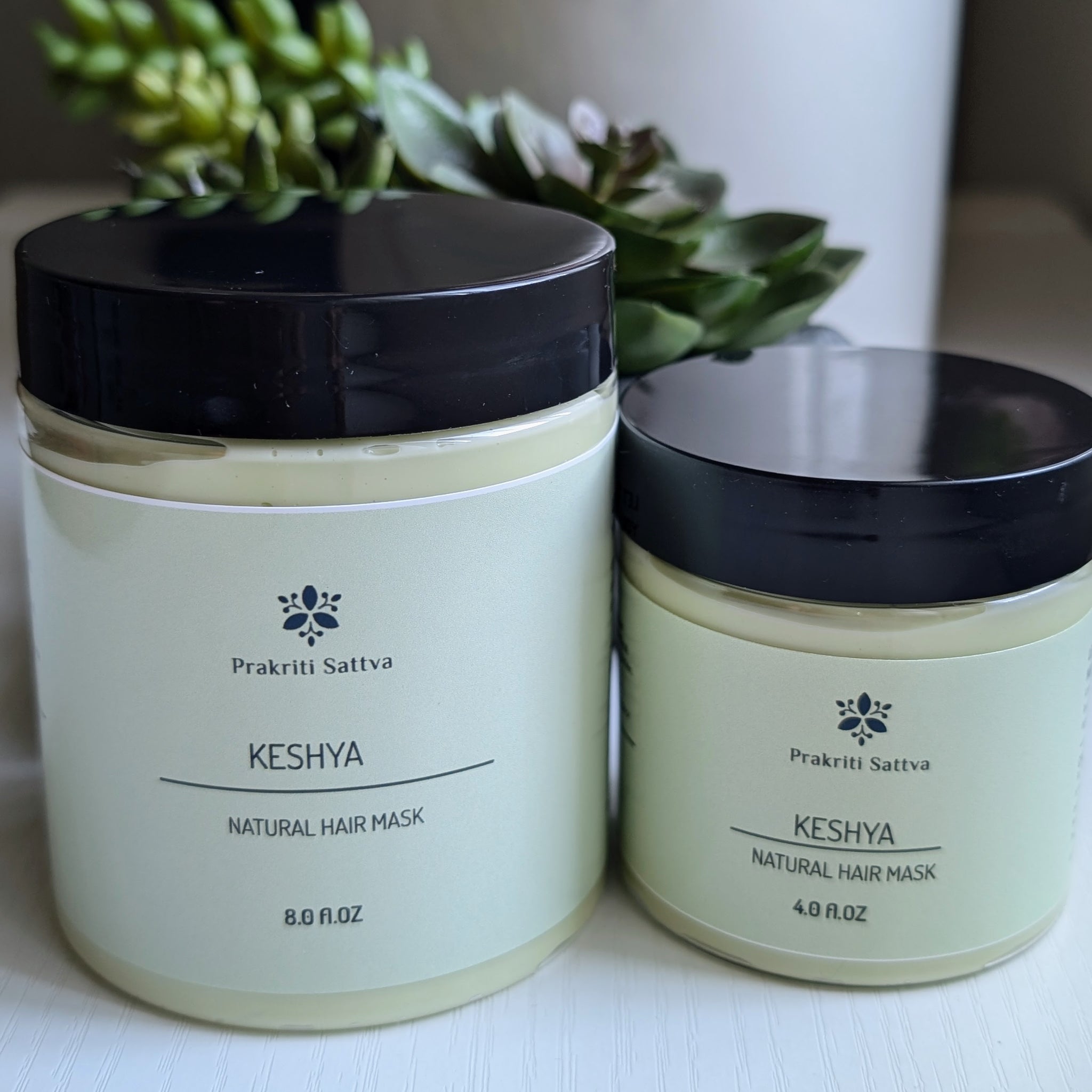 A four ounce jar and eight ounce jar of Prakriti Sattva Natural Deep Conditioning Hair Mask. The jars are filled with a creamy, green product. There is a succulent plant on the side.