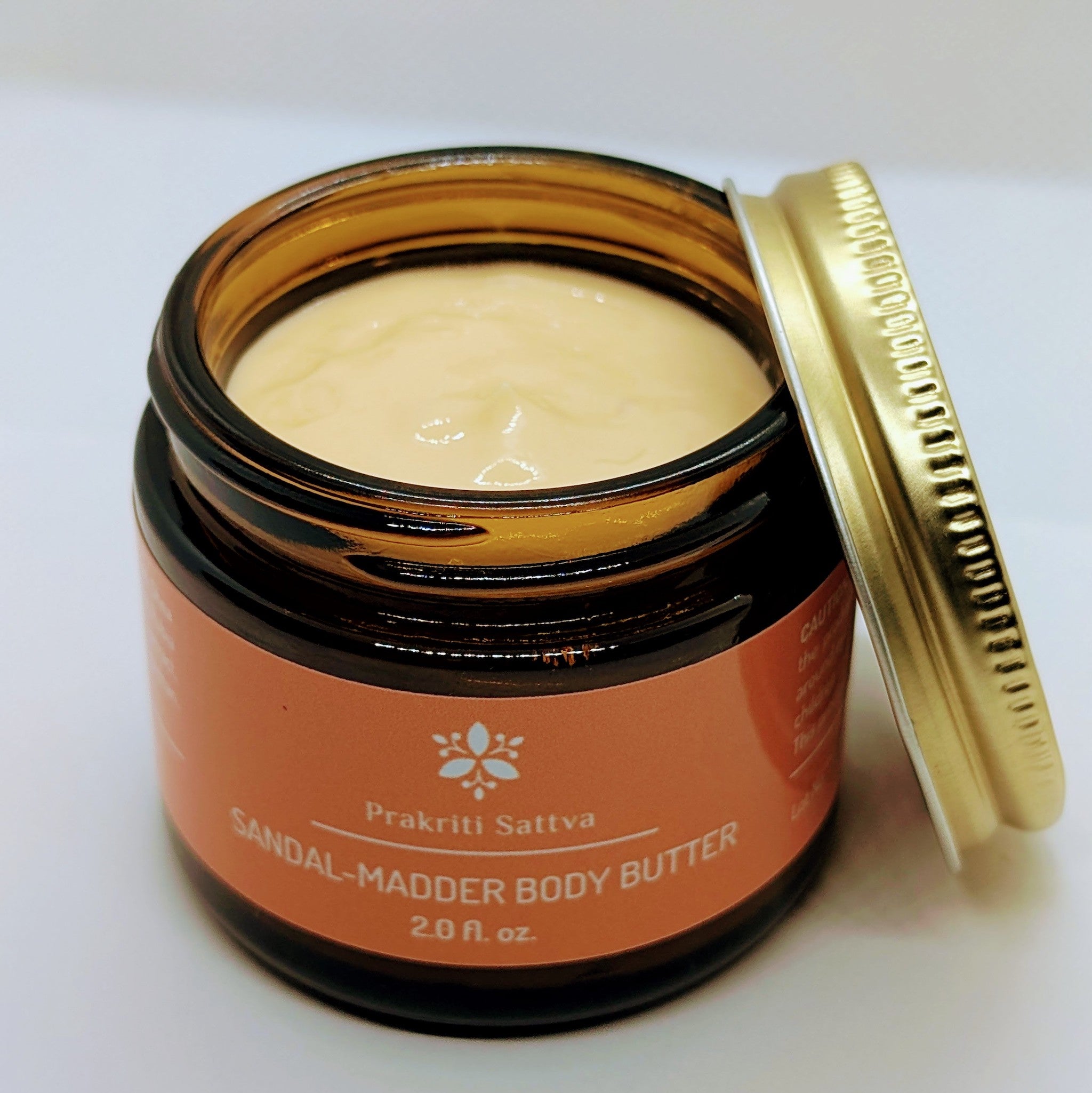 Jar of two ounce Prakriti Sattva Sandalwood Madder Body Butter with open lid on a white background