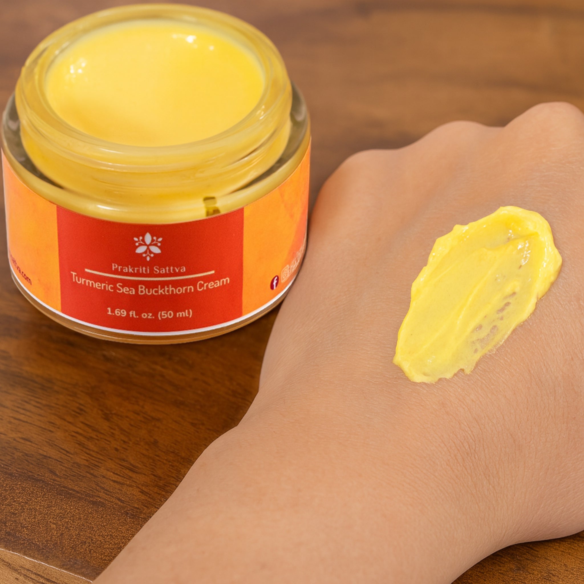 Jar of Prakriti Sattva Turmeric Sea Buckthorn Cream with a sample on a hand against a wooden background