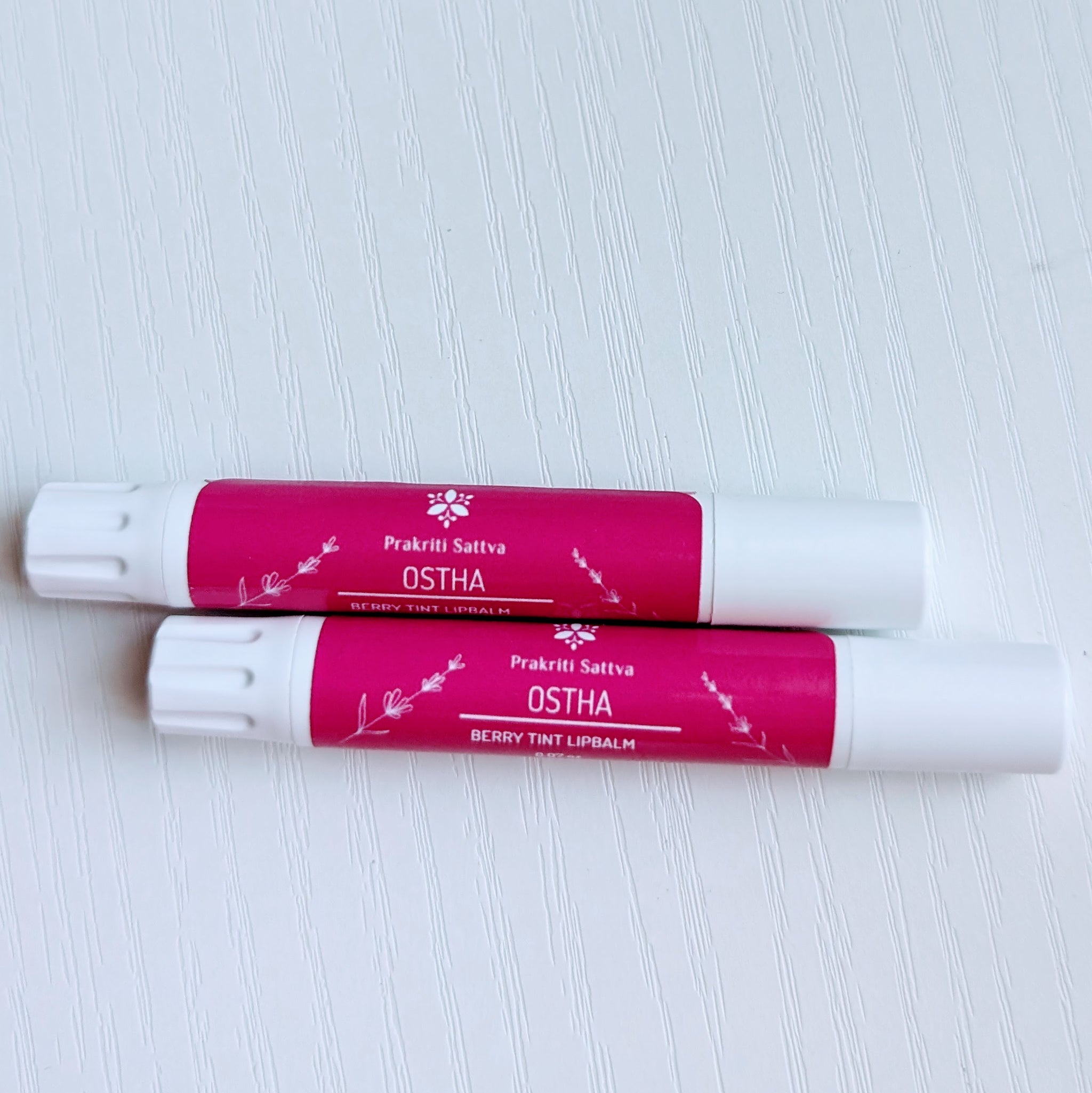 Prakriti Sattva Natural Berry Tinted Lip Balm. A tube of lip balm with a natural berry tint. The label features Ayurvedic symbols and herbs, including alkanet root, indicating the natural ingredients used.