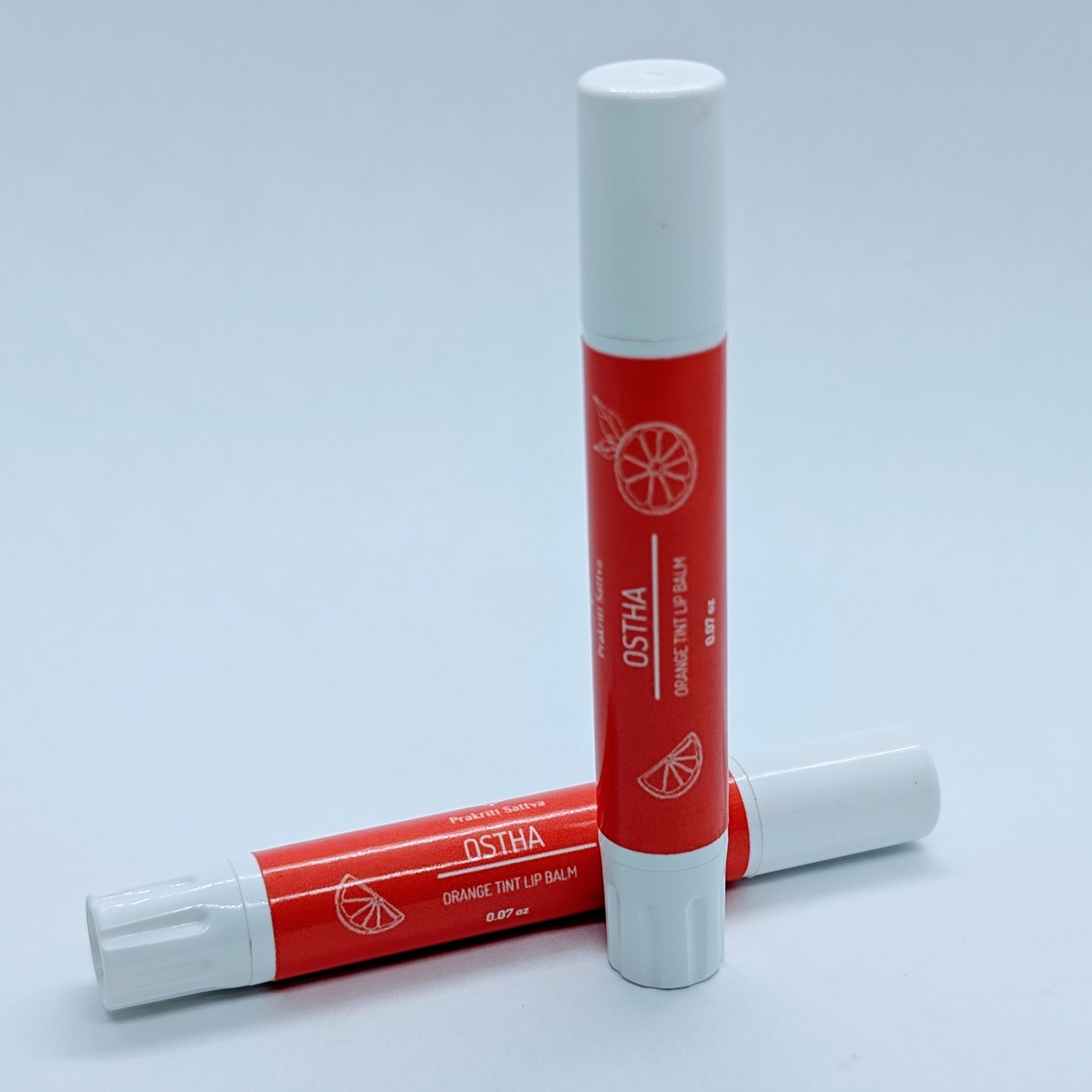 Prakriti Sattva Natural Berry Tinted Lip Balm. A tube of lip balm with a natural berry tint. The label features Ayurvedic symbols and herbs, including Manjistha root, orange, and patchouli, indicating the natural ingredients used.