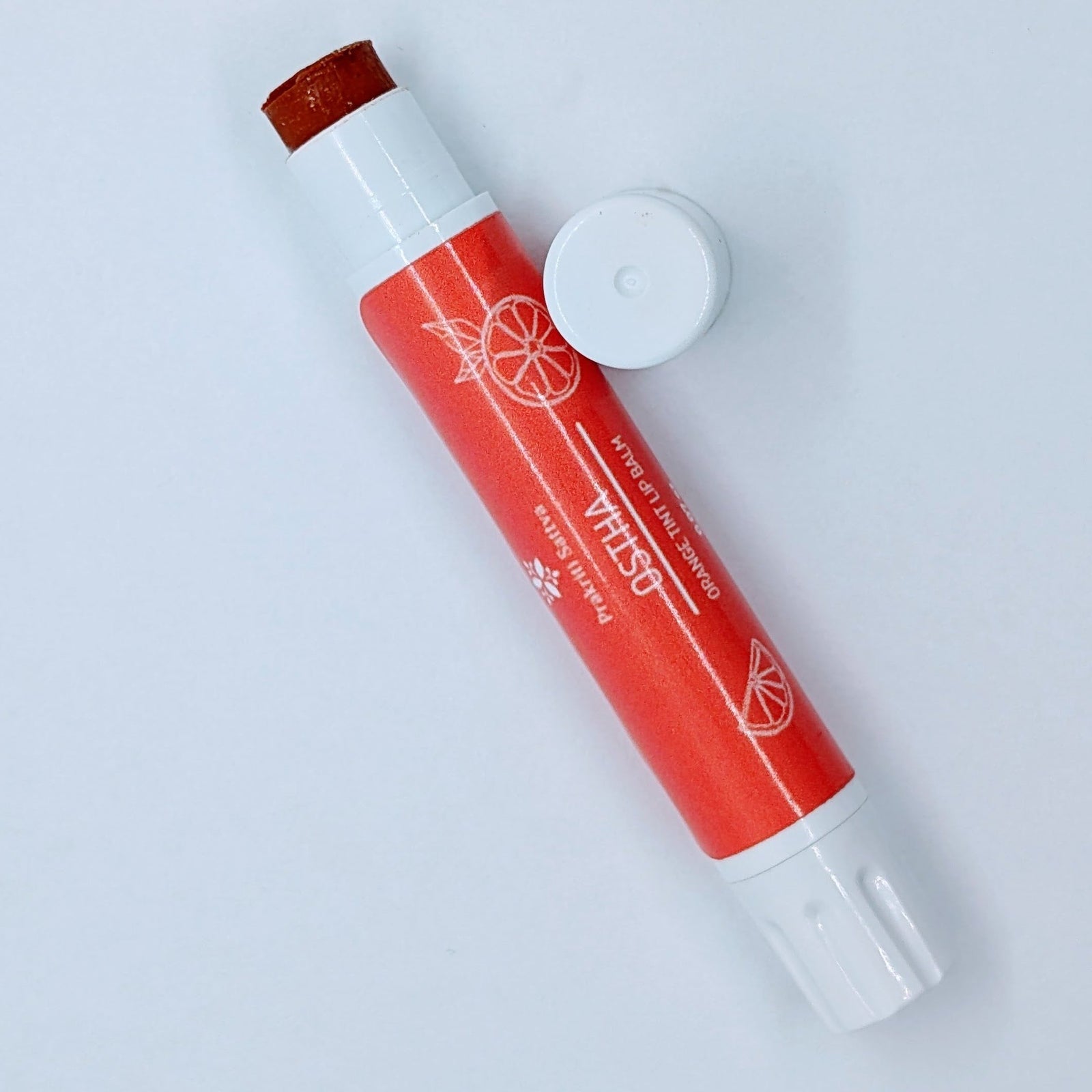 Prakriti Sattva Natural Berry Tinted Lip Balm. A tube of lip balm with a natural berry tint. The label features Ayurvedic symbols and herbs, including Manjistha root, orange, and patchouli, indicating the natural ingredients used.