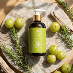Eight ounce Bottle of Prakriti Sattva Keshya Rosemary Amla Ayurvedic hair oil on a stone plate with green amla fruits and rosemary herb