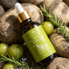 Prakriti Sattva Keshya Rosemary Amla Ayurvedic hair oil amber glass dropper bottle with green label on stones and gooseberries background