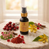 A bottle of Prakriti Sattva Glow & Bighten Serum stands on a marble surface with a small bowl of reddish manjistha (Indian madder root) powder, red rosehip berries, Licorice sticks, and yellow flowers around it.