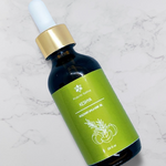 A dark amber bottle filled with Prakriti Sattva Rosemary Amla Hair Oil. The label features Ayurvedic symbols and herbs, including rosemary, amla, bhringaraj, and licorice, indicating the natural ingredients used.