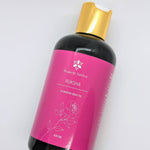 A glass bottle filled with Prakriti Sattva Ruksha Ayurvedic Body Oil for Dry Skin. The label features the brand name "Prakriti Sattva" and mentions "Dry Skin." It also features Ayurvedic herbs, including alkanet extract and lavender essential oil, indicating the natural ingredients used.