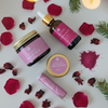 Prakriti Sattva Ruksha body butter, Body oil, Rose face pack and lip balm products with pink labels on a white surface with rose petals and hawthorn berries.