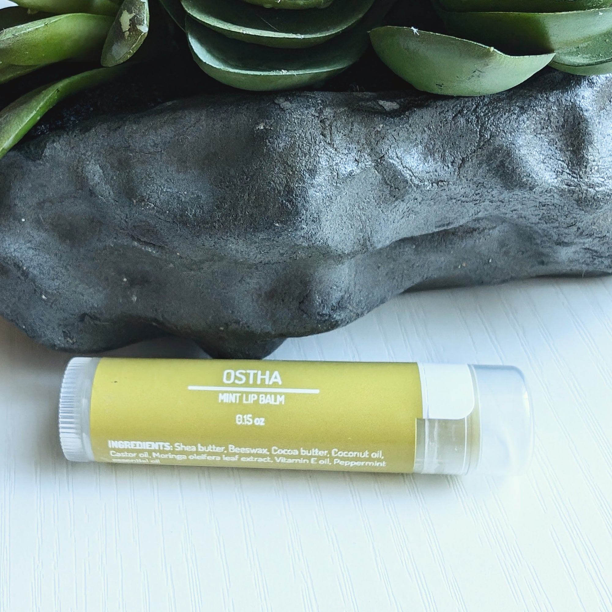 Ayurvedic natural lip balm with moringa extract and peppermint essential oil. It is a tube of lip balm with a natural, earthy color. The label features Ayurvedic symbols and herbs, including moringa and peppermint, indicating the natural ingredients used.