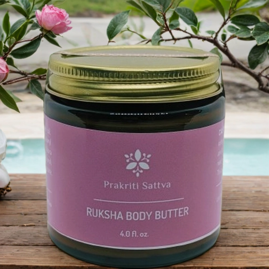 Four ounce Jar of Prakriti Sattva Ruksha Body Butter on a wooden surface with flowers in the background