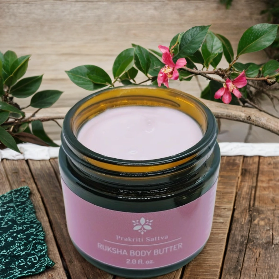 Two ounce amber glass Jar of Prakriti Sattva Ruksha Body Butter on a wooden surface with greenery in the background