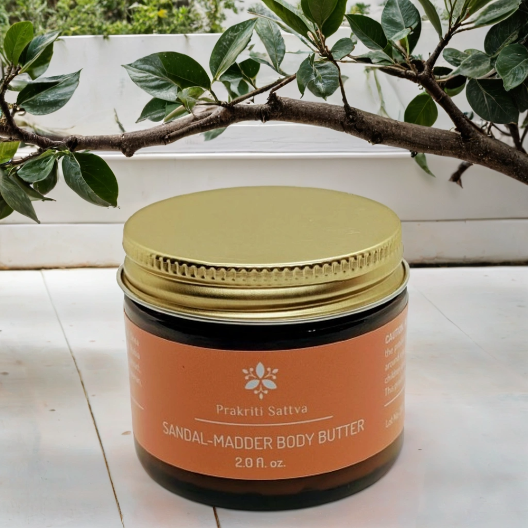 Jar of Prakriti Sattva Sandal Madder Body Butter on a wooden surface with greenery in the background