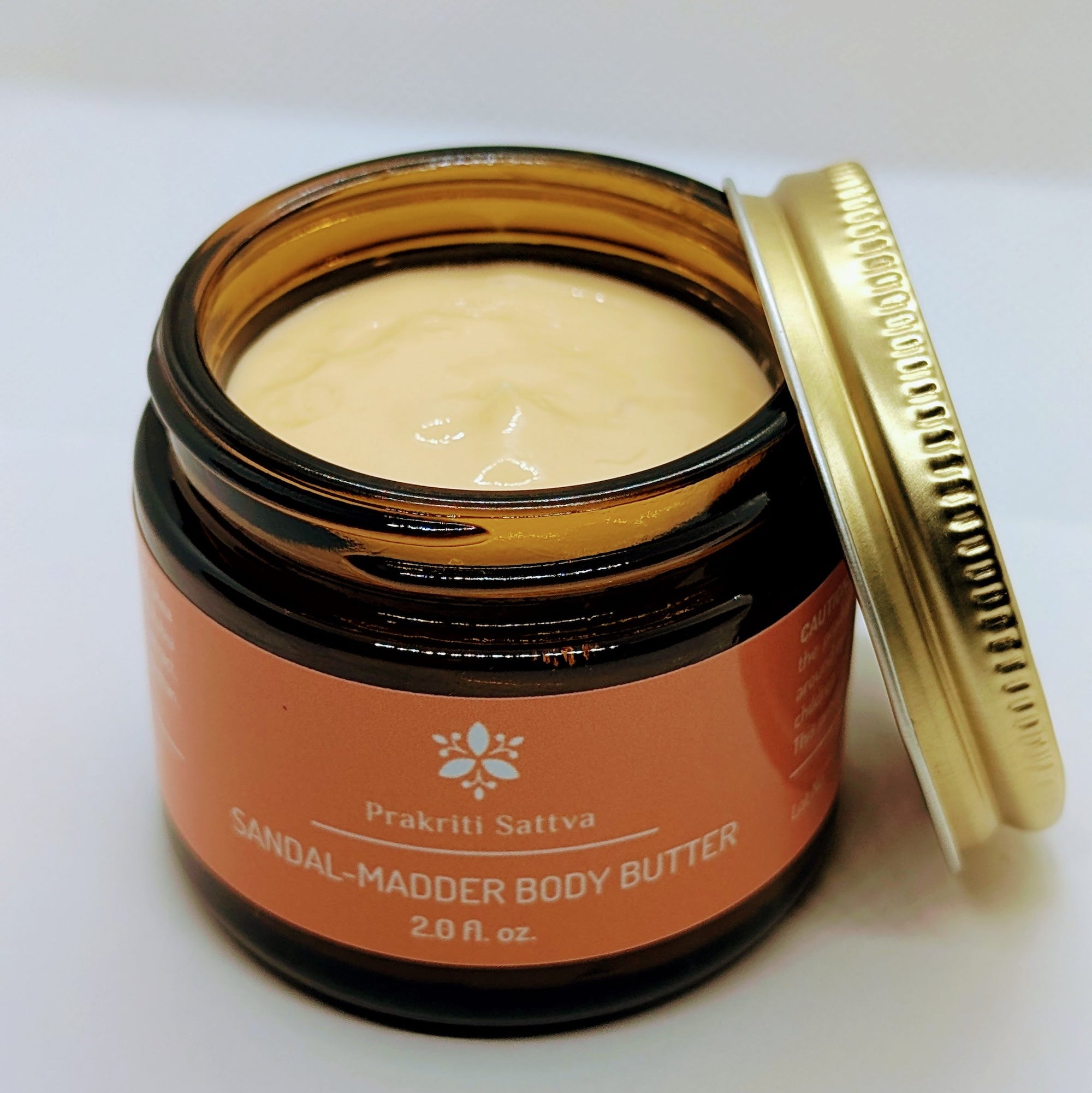 Jar of two ounce Prakriti Sattva Sandalwood Madder Body Butter with open lid on a white background