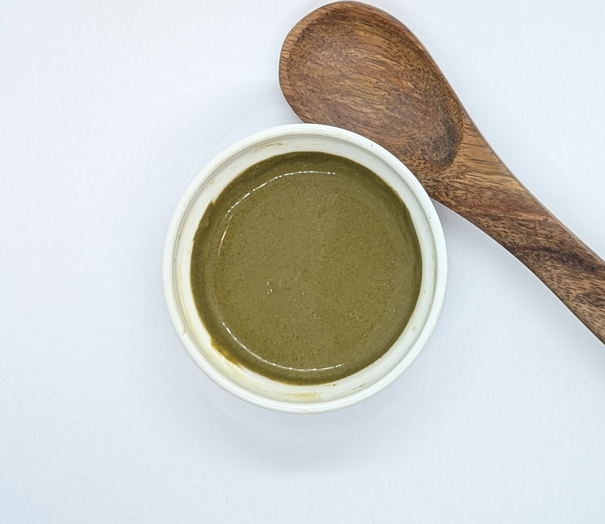 A white ceramic bowl of a paste made of Prakriti Sattva Neem Tulsi Moringa Amla Face Pack for Acne-Prone and Kapha-Pitta Skin. There is a wooden spoon on the side of the bowl. A natural, Ayurvedic face mask to help reduce acne, balance oil production, and soothe inflammation.