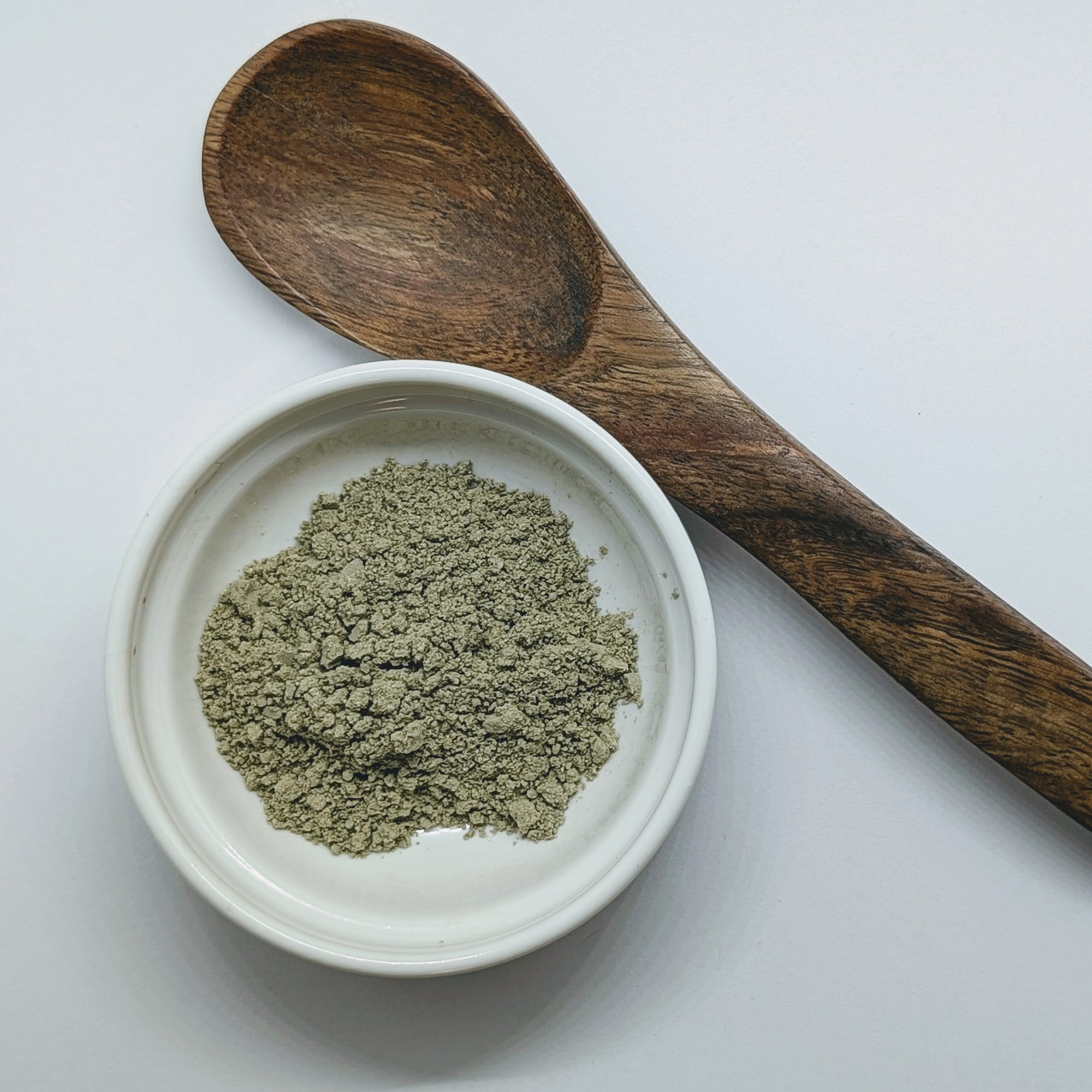 A scoop of Prakriti Sattva Neem Tulsi Moringa Amla Face Pack for Acne-Prone and Kapha-Pitta Skin in a ceramic white bowl and a wooden spoon on the side. A natural, Ayurvedic face mask to help reduce acne, balance oil production, and soothe inflammation.